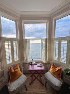 a living room with two chairs and a table and windows at Môr Heli Guest House Criccieth in Criccieth