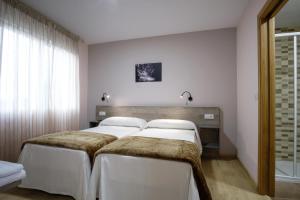 two beds in a bedroom with white walls at Albergue Pensión Cima do Lugar in Arzúa