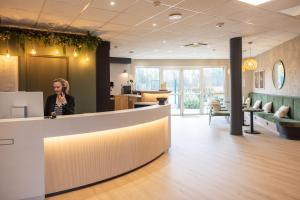 a woman standing behind a counter in a lobby at Brit Hotel Saint-Méen-le-Grand en Brocéliande in Saint-Onen-la-Chapelle