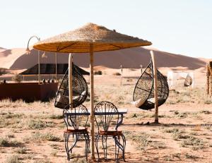 a table and chairs under an umbrella in the desert at Desert Paradise Lodging in Merzouga