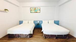 two beds in a room with white walls and wood floors at 小逗民宿 in Taitung City