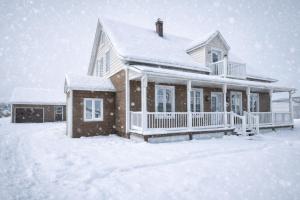 a house covered in snow in a yard at La belle ancestrale in Sainte-Anne-des-Monts