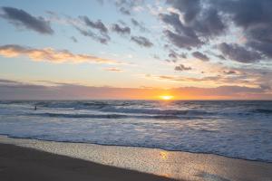 a sunset on the beach with a person in the ocean at Atlantic Selection - Studio La Sud - Piscine in Hossegor