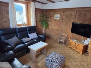 a living room with a black leather couch and a tv at Chasa Bellavista in Ardez