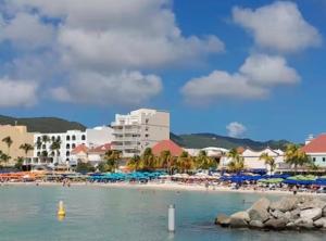 a beach with people and umbrellas and buildings at Panoramic Ocean View Flat-St Maarten in Philipsburg
