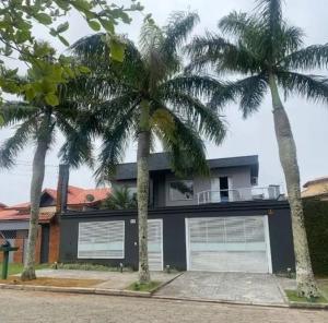 a house with two palm trees in front of it at Casa de temporada com piscina in Peruíbe