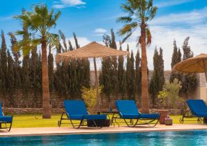 a pool with chairs and umbrellas and palm trees at Dar Ayman Essaouira in Essaouira