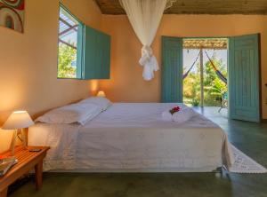 a bedroom with a bed and a table and windows at Chalé Pé de Araçá - Massarandupió in Entre Rios
