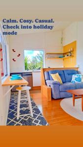 a living room with a blue couch and a table at Redshed Studio Mangawhai in Mangawhai