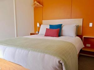 a bedroom with a large bed with two colorful pillows at Redshed Studio Mangawhai in Mangawhai