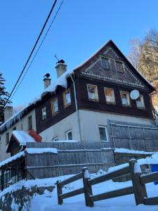 a house covered in snow with a fence in front at Sauna Chata BedRich in Bedřichov