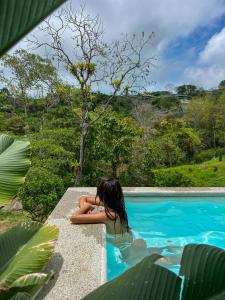 a woman sitting on a ledge next to a swimming pool at Dar Lamia Boutique Hotel - Adults Only in Manuel Antonio