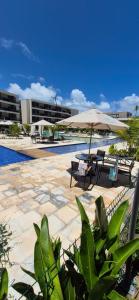 a patio with tables and an umbrella and a pool at Flat Malia Beach 005A in Porto De Galinhas