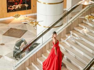 a woman in a red dress walking down stairs talking on a cell phone at Raffles Istanbul in Istanbul +182 photos