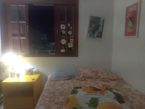 a bedroom with a bed with a night stand and a window at Hostel casa amarela in Rio das Ostras