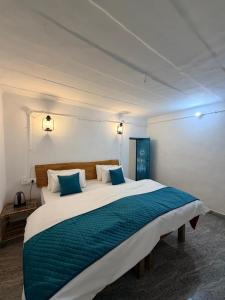 a bedroom with a large white bed with blue pillows at NAMOH e VIRAASAT in Chopta