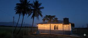 a small house with lights on it next to two palm trees at Thulir Farm Stay Near Isha Yoga Adiyogi in Coimbatore