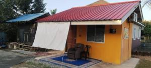 a small house with a red roof and a chair at KAMI roomstay 2 in Kampong Banggol Lalang