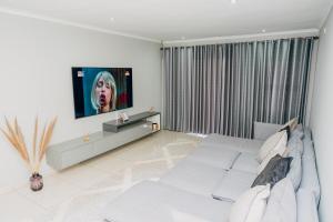 a white living room with a white couch and a tv at Elle Residence in Gaborone