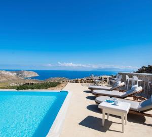 a pool with chairs and the ocean in the background at Amallini Suites Mykonos in Super Paradise Beach