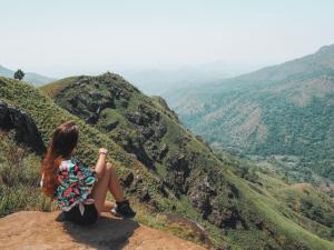 a woman sitting on the edge of a mountain looking at the valley at oasis in Ella
