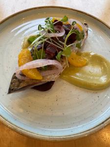 a plate with a piece of fish with vegetables and a pickle at The Hare and Hounds in Fulbeck
