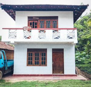 a white house with wooden windows and a blue truck at Indrasiri Villa Midigama in Kumbalgama