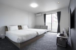 a white bedroom with a large bed and a window at Laon Inn Miyakojima in Miyako-jima