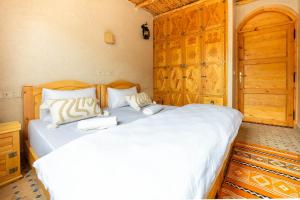 a bedroom with two white beds and a wooden door at Berber Surf House in Tamraght Ouzdar