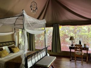 a bedroom with a canopy bed with a desk and a window at Ikweta Safari Camp in Kinna