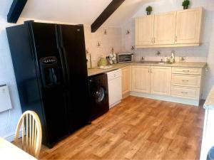 a kitchen with a black refrigerator and wooden floors at Rosecraddoc Manor - Coachman's in Saint Cleer