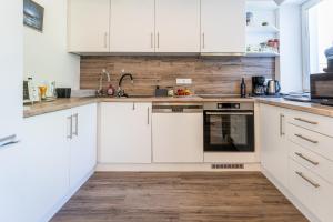 a kitchen with white cabinets and a wooden floor at KJB Vendégház Dombori in Fadd-Dombori +3 photos