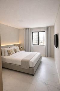 a white bedroom with a large bed and a window at Summerview novo , 2 piscinas e 2 jacuzzis, 2 quartos Novo! in Itapema