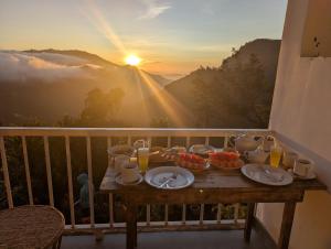 a table with plates of food on a balcony with the sunset at Rock Paradise Homestay in Ella