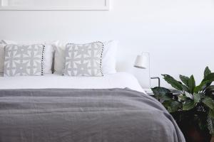 ein Schlafzimmer mit einem weißen Bett, Kissen und einer Pflanze in der Unterkunft Bask & Stow I Luxe Guesthouse in Byron Bay