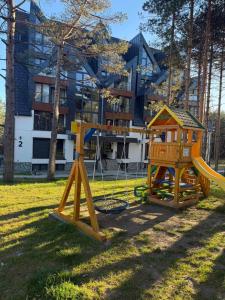 two playground equipment in a park with a building at MONA Apartman - Šumska Oaza in Divčibare