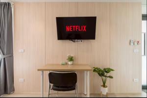 a television on a wall with a table and a chair at Ningle Place Hotel Pathumthani in Ban Pak Khlong Si