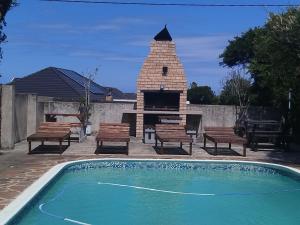 a brick fireplace and a swimming pool with benches and a grill at Palm Tree BnB in East London +19 photos
