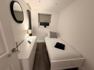 a small white room with a bed and a mirror at Adrian Cottage in Abbots Langley