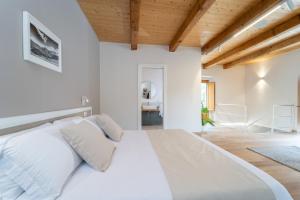 a white bedroom with a large white bed and wooden ceilings at Le Vie del Borgo | 3 dimore indipendenti a Civita in Civita