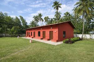 a red building in a field with palm trees at Manan Beach Resort in Malpe