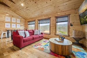 a living room with a red couch and a table at SmokiesBoutiqueCabins would love to host you at Dolly's Cute Cabin! 4 Suites with Private Bathrooms - Hot Tub, Fire Pit, Game Room, Resort Pool open Memorial Day through Labor Day! in Gatlinburg