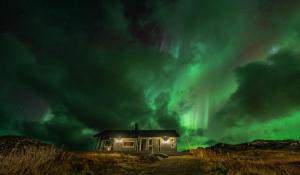 a house with the aurora in the sky at Lofoten Links Lodges in Gimsøy