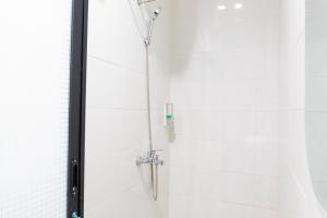 a shower in a bathroom with white tiles at Behomy Suhat Malang in Karangjepun