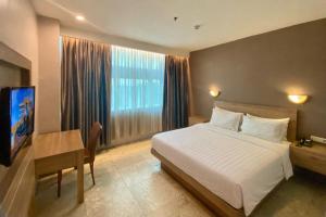 a bedroom with a bed and a desk and a television at Manna Hotel Pematangsiantar in Pematangsiantar