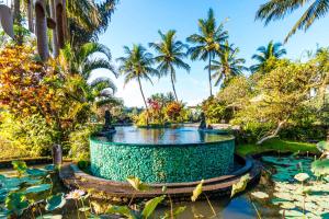 a fountain in a pond in a garden with palm trees at Villa Taman di Blayu by AGATA in Tabanan