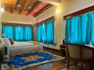 a bedroom with blue curtains and a bed and a desk at sinchula Villa Resort in Paro