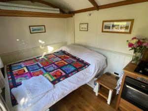a small bedroom with a bed with a quilt on it at Dartmoor Shepherds Hut at The Shrubbery, River Walkham, Horrabridge, Yelverton in Tavistock