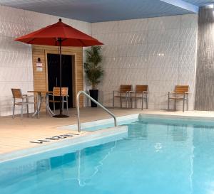 a swimming pool with an umbrella and a table and chairs at Hôtel WelcomInns in Boucherville