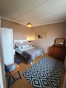 a bedroom with a bed and a chair and a rug at Haus Windhoek - Charming Coastal Escape in Struisbaai